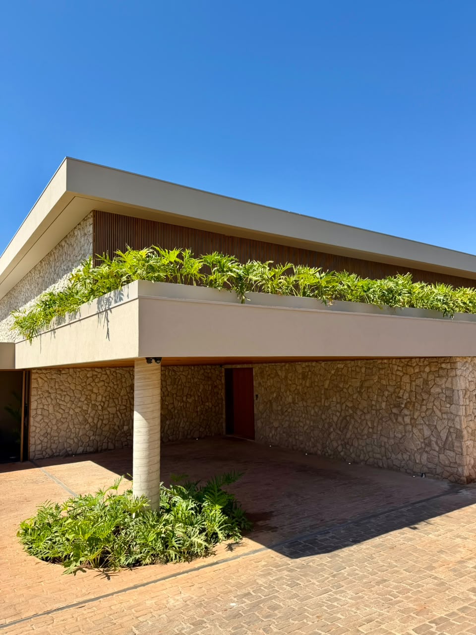 Entrada da casa com pórtico, parede de pedra e jardim
